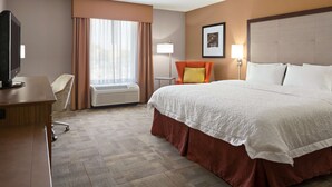 Habitación de hotel con cama, escritorio, silla, lámpara y un cuadro en la pared.