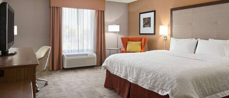 A hotel room with a bed, a desk, a chair, a lamp, and a picture on the wall.