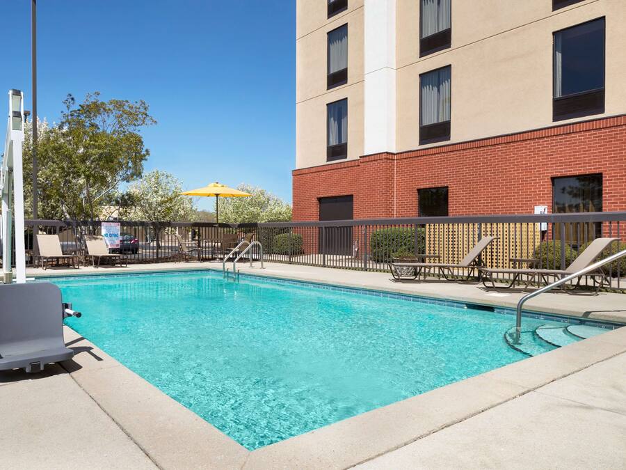 A rectangular swimming pool with clear blue water, surrounded by a metal fence. There are lounge chairs and a yellow umbrella near the pool.