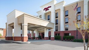 Un hotel con entrada cubierta, un letrero destacado y una bandera estadounidense.