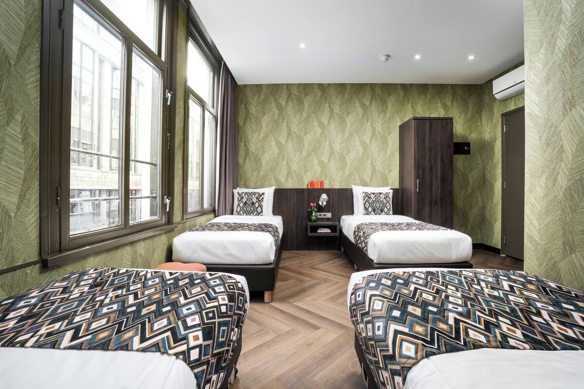 Habitación de hotel con dos camas, un armario, una mesita con una radio y ventanas amplias.