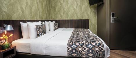 A modern hotel room with a large bed, a flat-screen TV mounted on the wall, and a wooden floor.