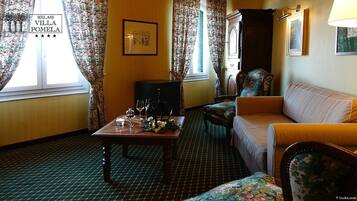 A hotel room with a dining table set with glasses and a vase, a sofa, a chair, and a cabinet.