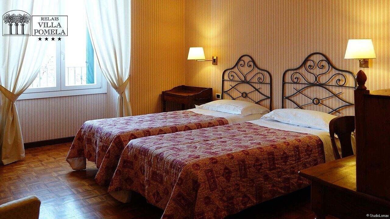 Ett hotellrum med två sängar, ett skrivbord i trä och ett fönster med gardiner.
