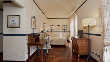 Une chambre d’hôtel avec un plancher en bois, un lit recouvert d’une courtepointe à motifs, un bureau avec une chaise, une commode et une lampe.