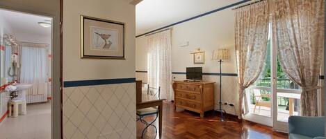 A room with a wooden floor, a dresser, a television, and a window with curtains.