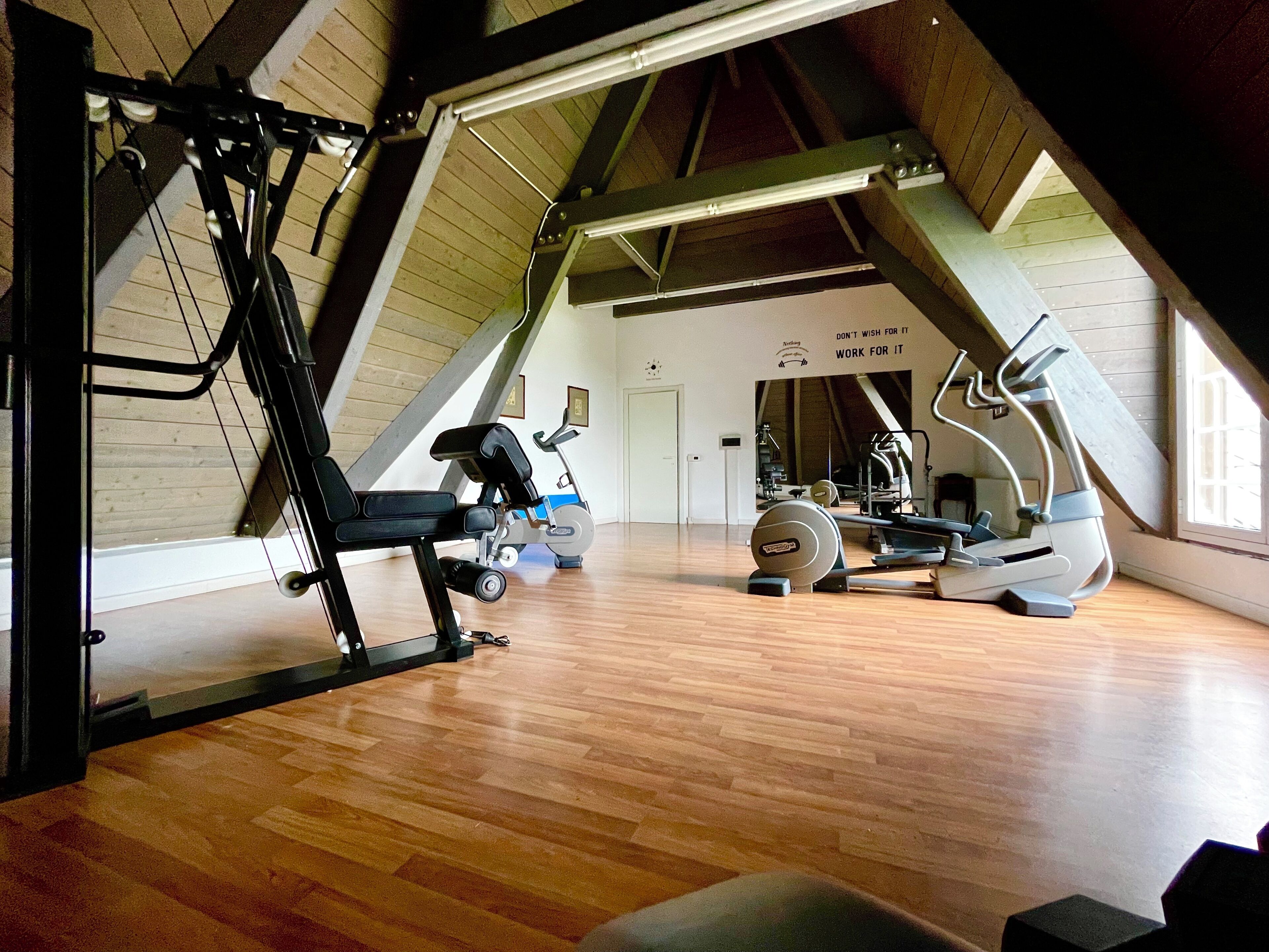 Een sportzaal in zolderstijl met houten vloeren, fitnessapparatuur en een schuine kap.