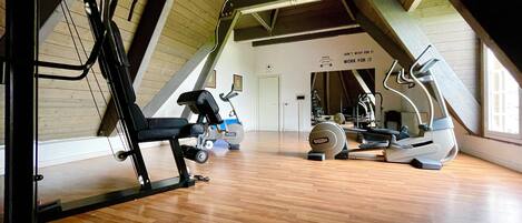 Un gimnasio estilo ático con suelos de madera, equipo de ejercicio y techo inclinado.