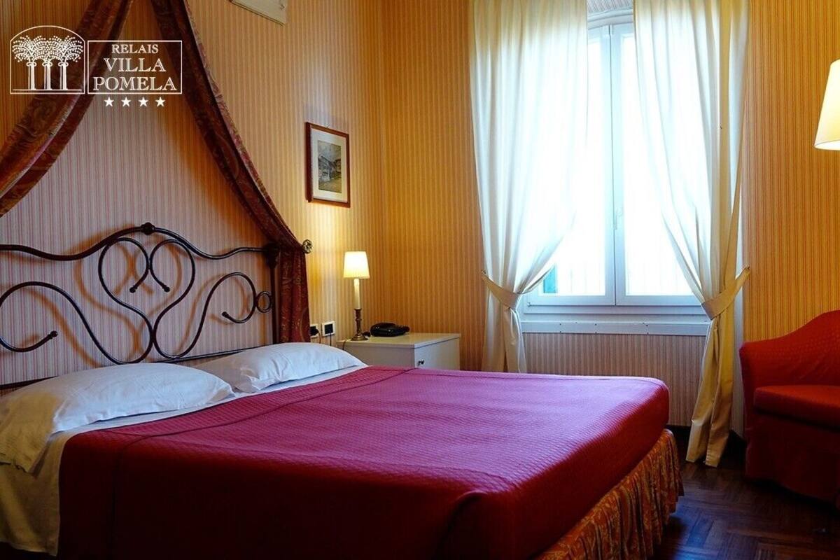 A hotel room with a bed, a nightstand, a lamp, a chair, and a window with curtains.