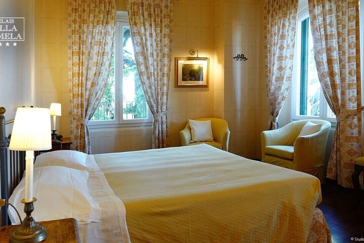 A hotel room with a bed, two chairs, a lamp, and a window with curtains.
