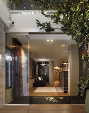 Un interior moderno con puerta de vidrio, un sofá negro, piso de madera y un tapete decorativo.