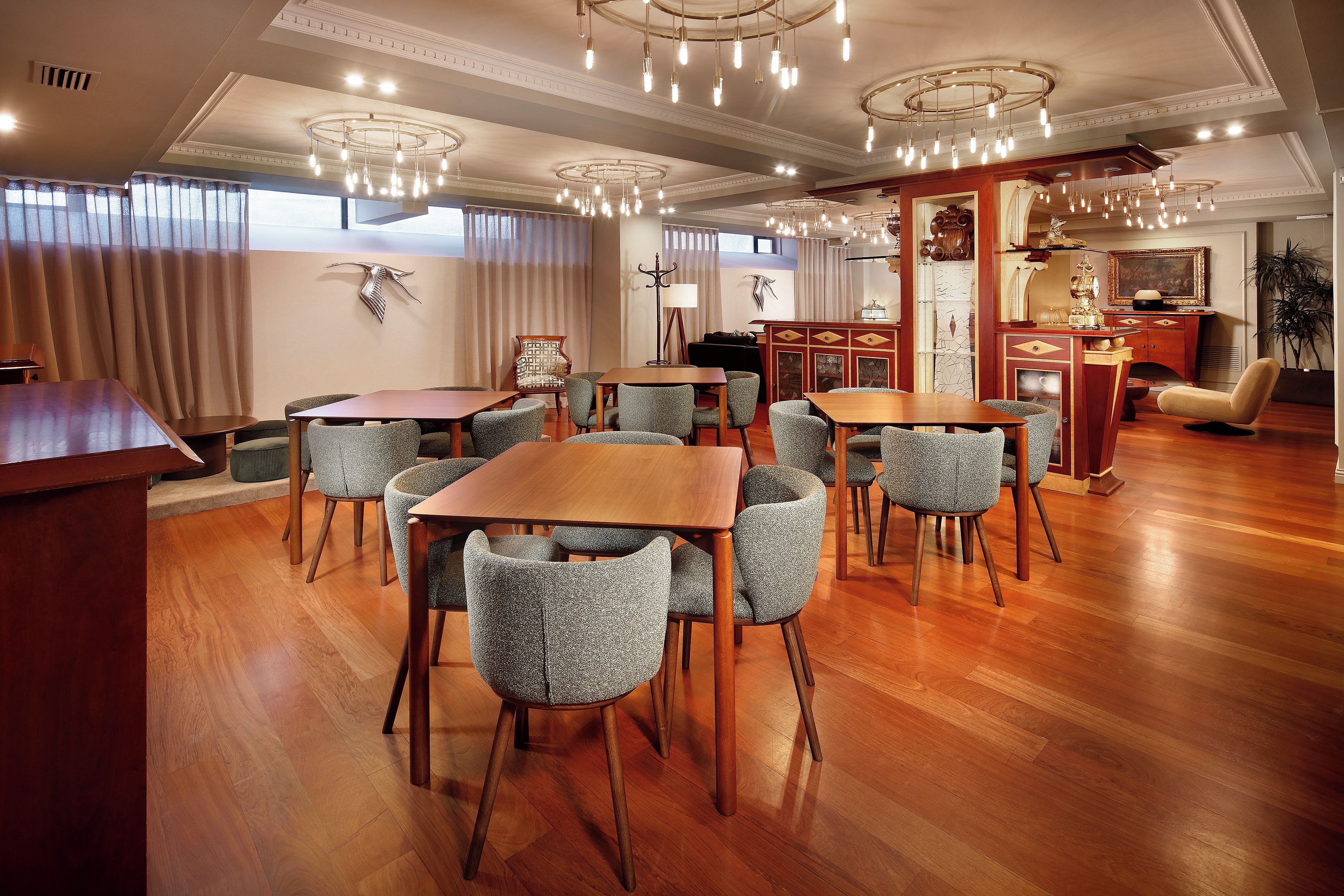 A dining area with wooden tables and chairs, a bar area with a mirror and decorative items, and a seating area with a sofa and armchairs.