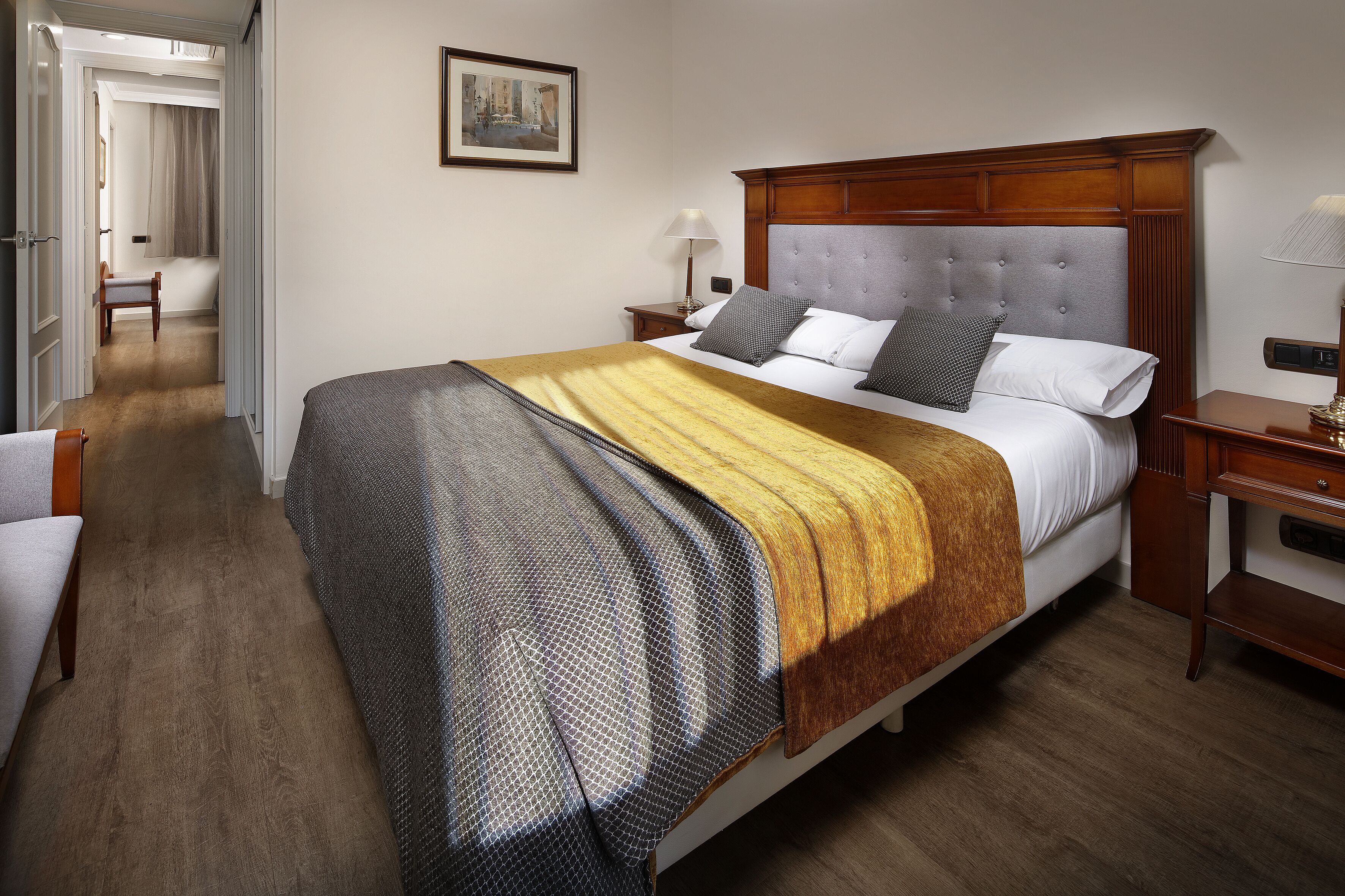 Een hotelkamer met een groot bed, een houten hoofdeinde, een nachtkastje met een lamp en een stoel in de hoek.