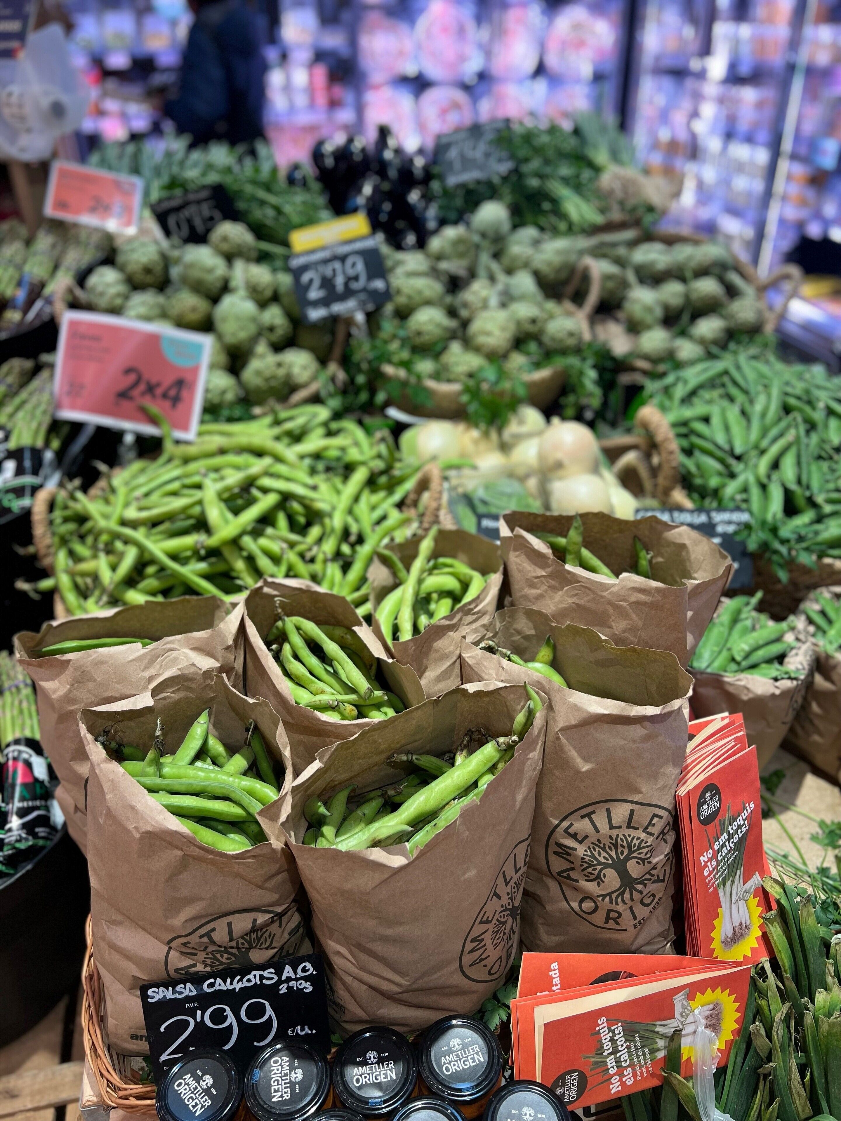 Un expositor de productos con judías verdes, alcachofas y otras verduras. Se ven los precios y las etiquetas.