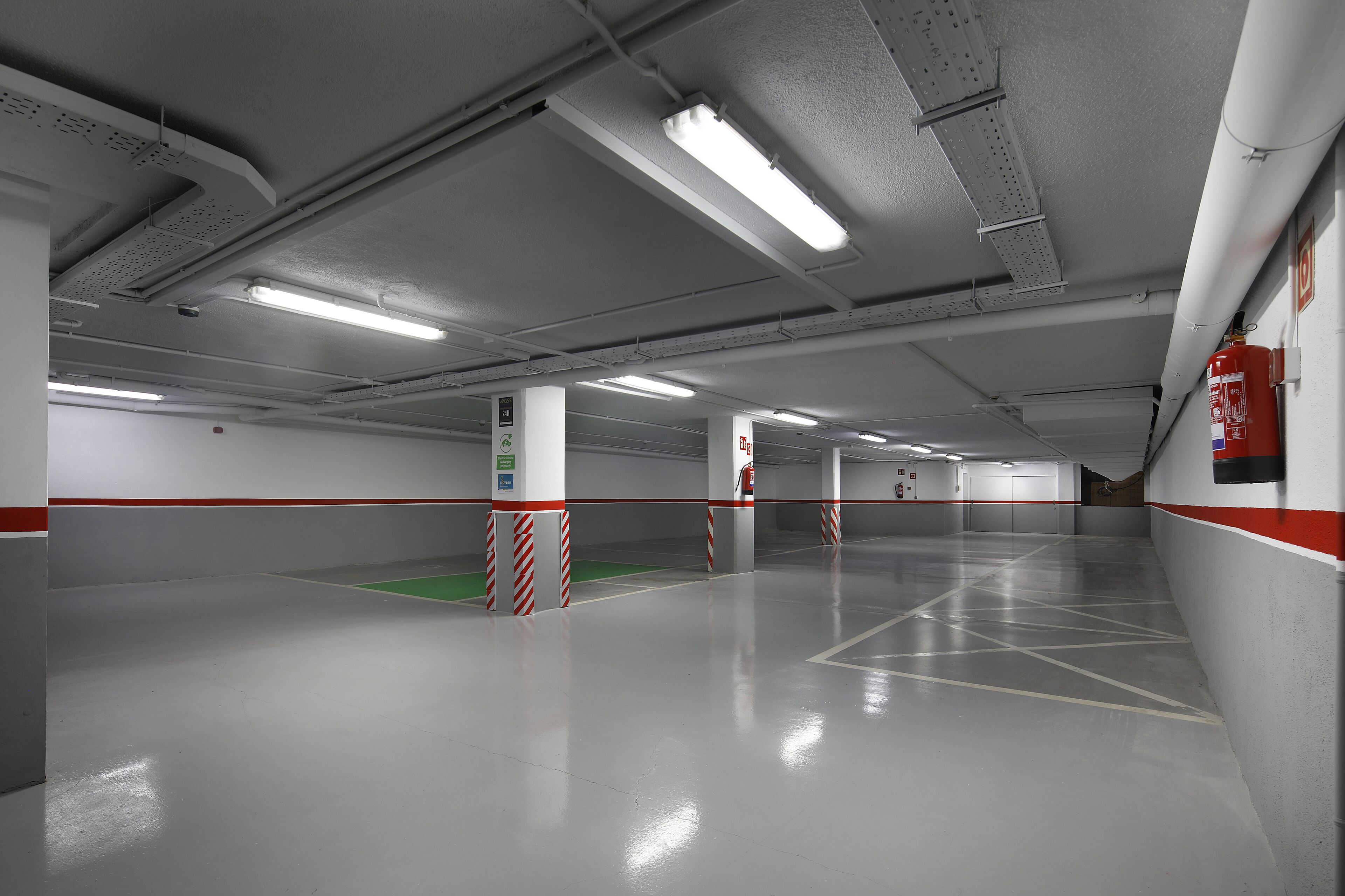 A clean, empty parking garage with white walls, red and white striped barriers, and fluorescent lighting.