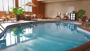 Una piscina interior con sillas de descanso y mesas, rodeada de plantas en macetas y un suelo de baldosas.