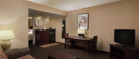 A hotel room with a sofa, a small table, a TV, a desk with a chair, a mirror, and a painting on the wall.
