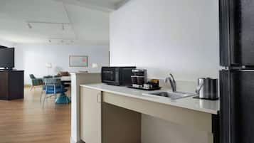 A modern kitchen with a microwave, coffee maker, and kettle. There is a dining area with chairs and a table.