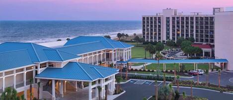 A hotel with a blue-roofed building, a parking lot, and a view of the ocean.