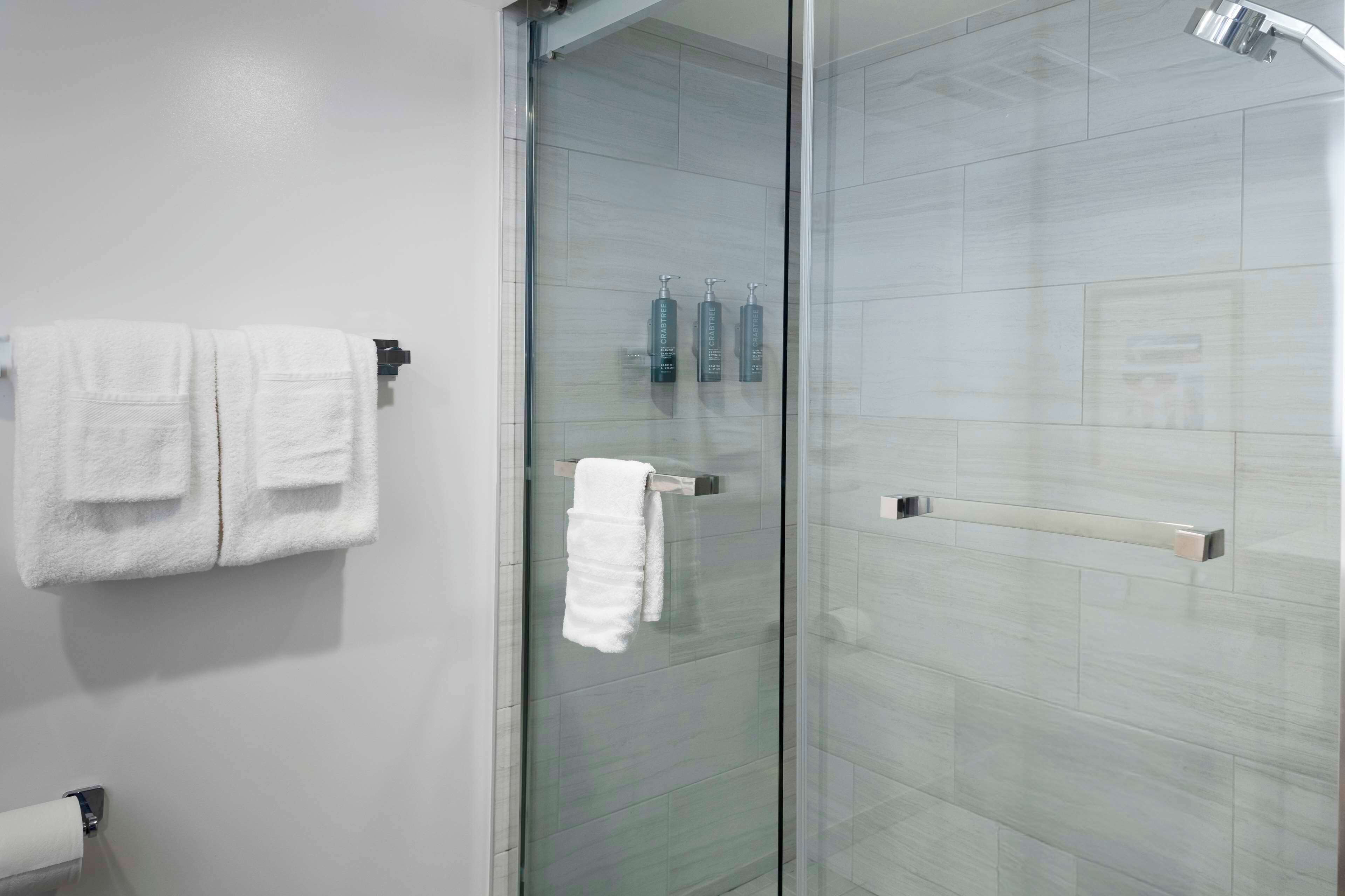 A bathroom with a glass shower door, white towels on a rack, and toiletries on the wall.