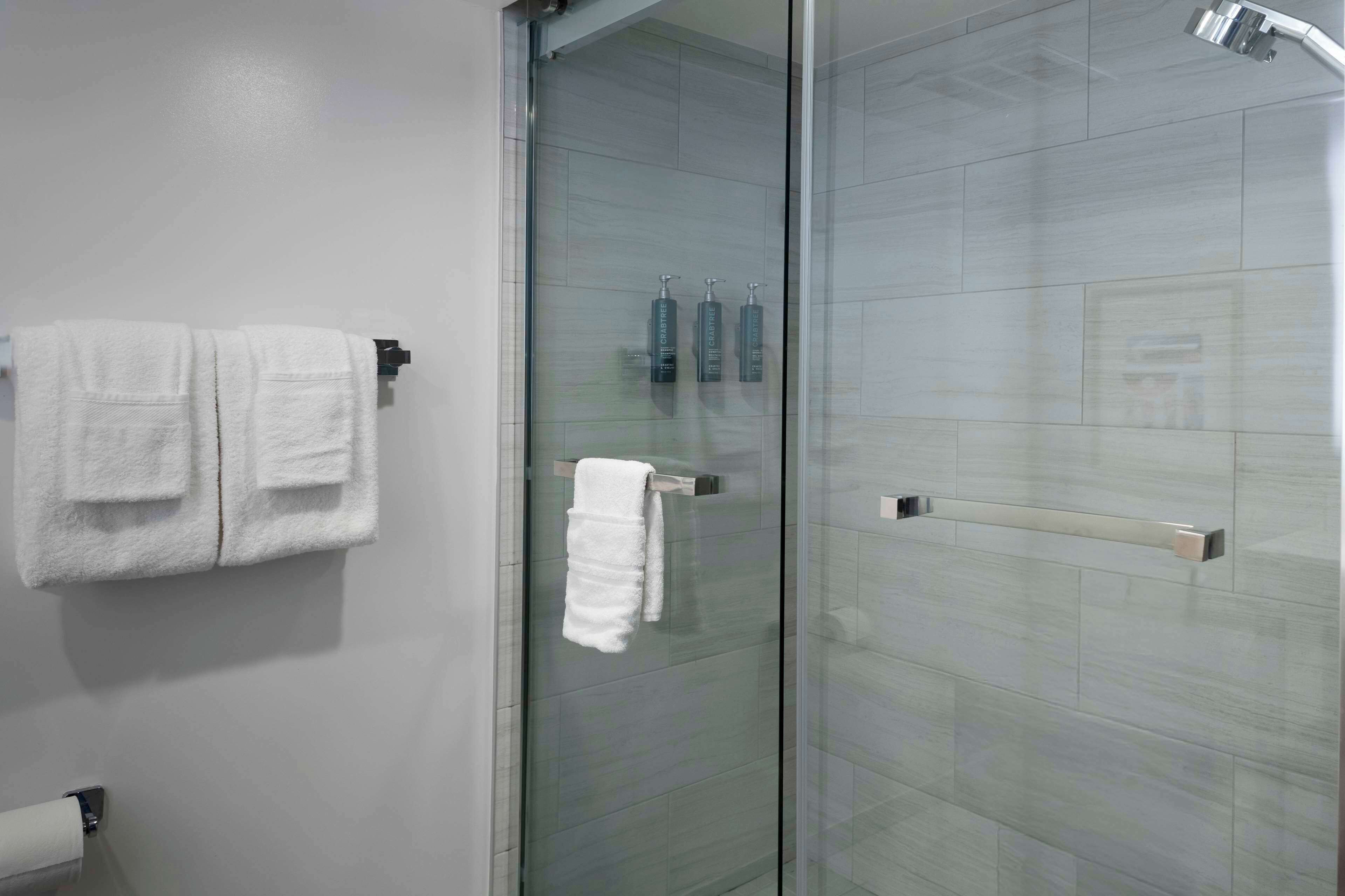 Une salle de bain avec une porte de douche en verre, des serviettes blanches et des articles de toilette fixés au mur.