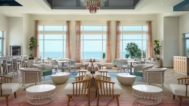 Spaziosa area lounge con vista sul mare, caratterizzata da tavoli rotondi, comodi posti a sedere e un soffitto decorato con motivi a foglia.