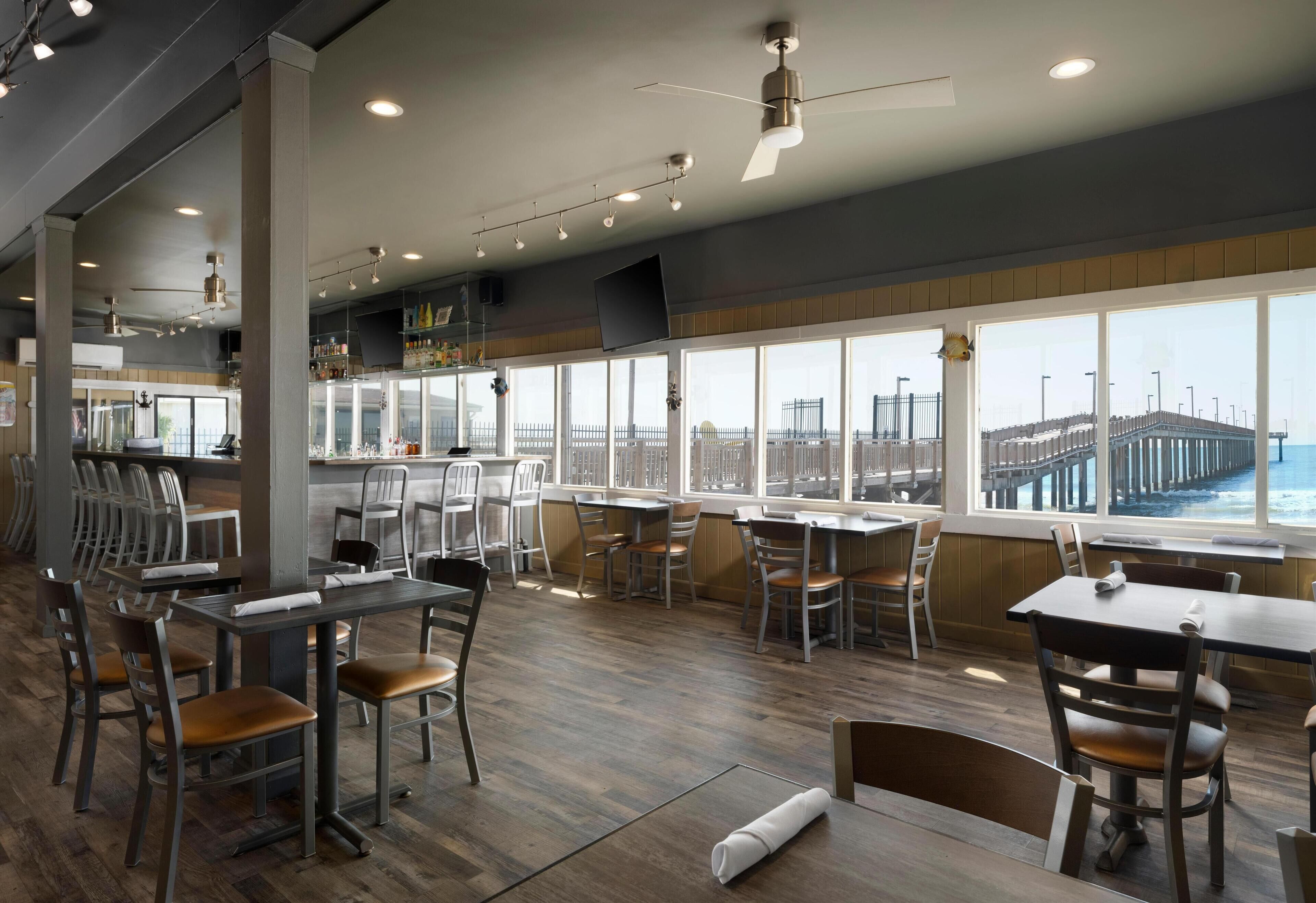 Restaurante com vista para um cais, piso de madeira e mobiliário moderno.
