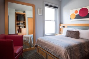 Una camera d'albergo con un letto, una sedia rossa, un armadio, uno specchio, una finestra e un quadro appeso al muro.