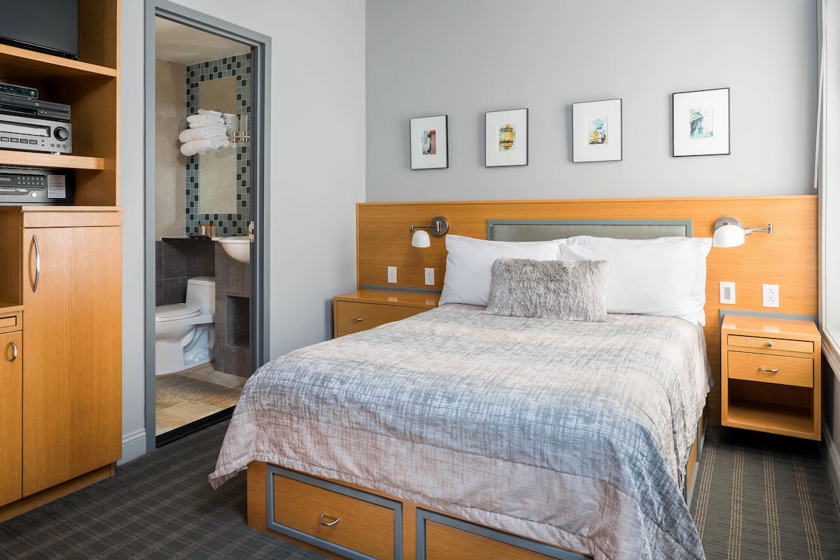 A hotel room with a bed, bedside tables, a wardrobe, a bathroom with a toilet and sink, and framed pictures on the wall.
