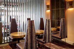 Een restaurantinterieur met hoge rugleunstoelen, ronde tafels en een gordijn met patroon.
