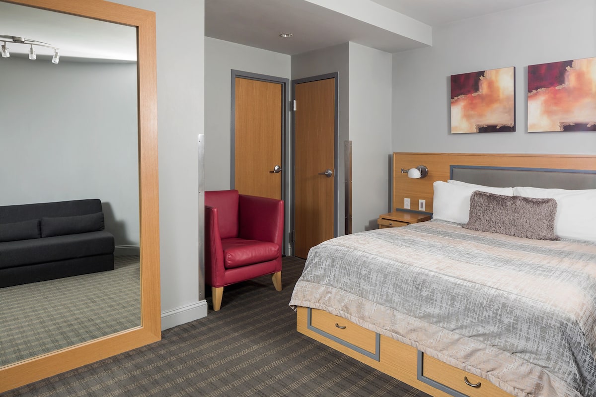 A hotel room with a bed, a red chair, a wardrobe, and a mirror.