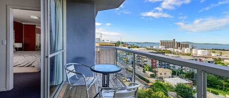 A balcony with a table and chairs, a bed, and a view of the city and water.