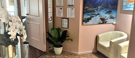 A reception area with a glass door, a potted plant, a seating area with chairs, and a wall with informational posters.