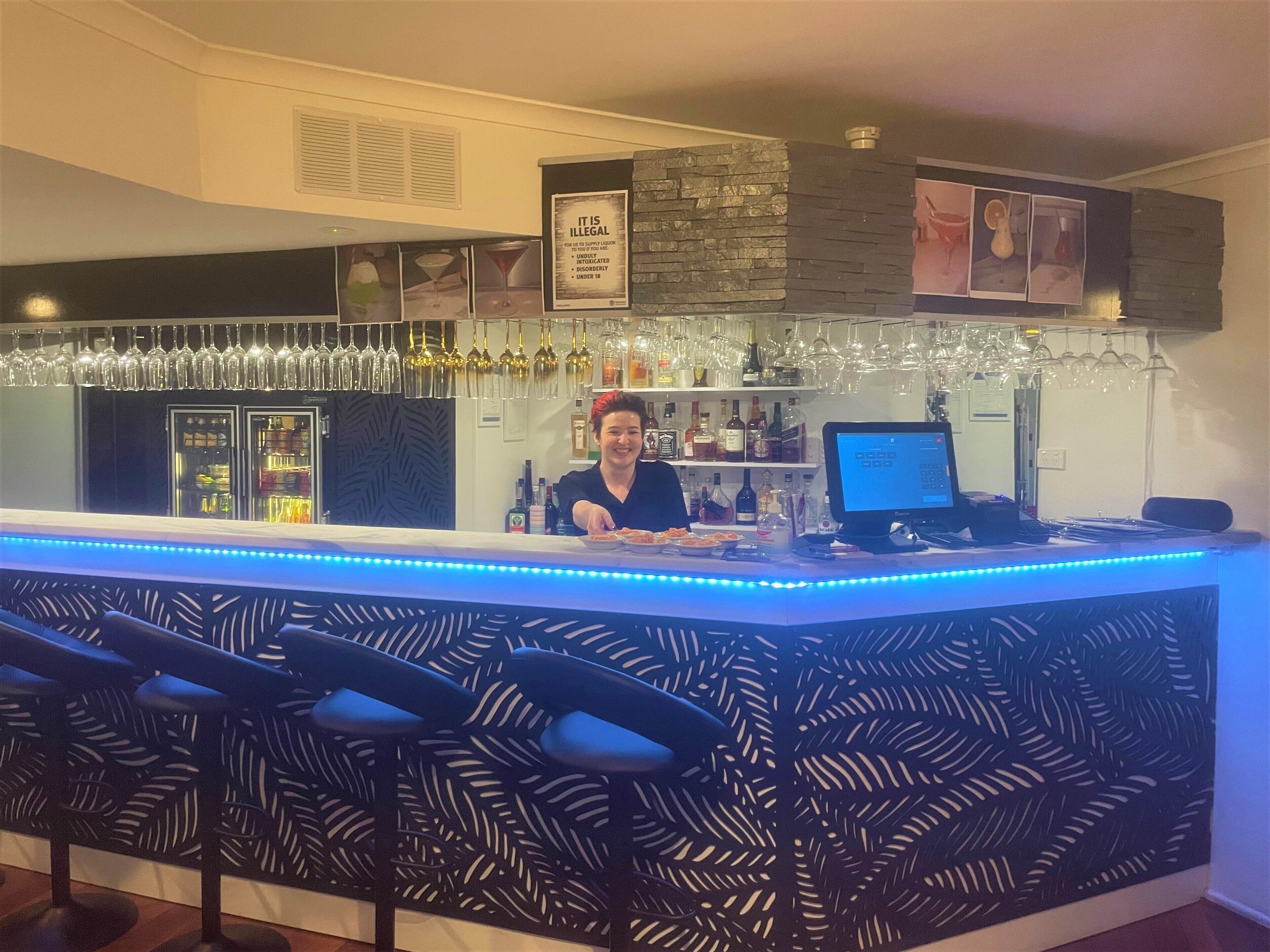 A bar area with a counter, bar stools, and a variety of bottles and glasses.