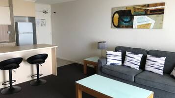 A modern living room with a grey sofa, two black bar stools, a wooden coffee table, and a painting on the wall.