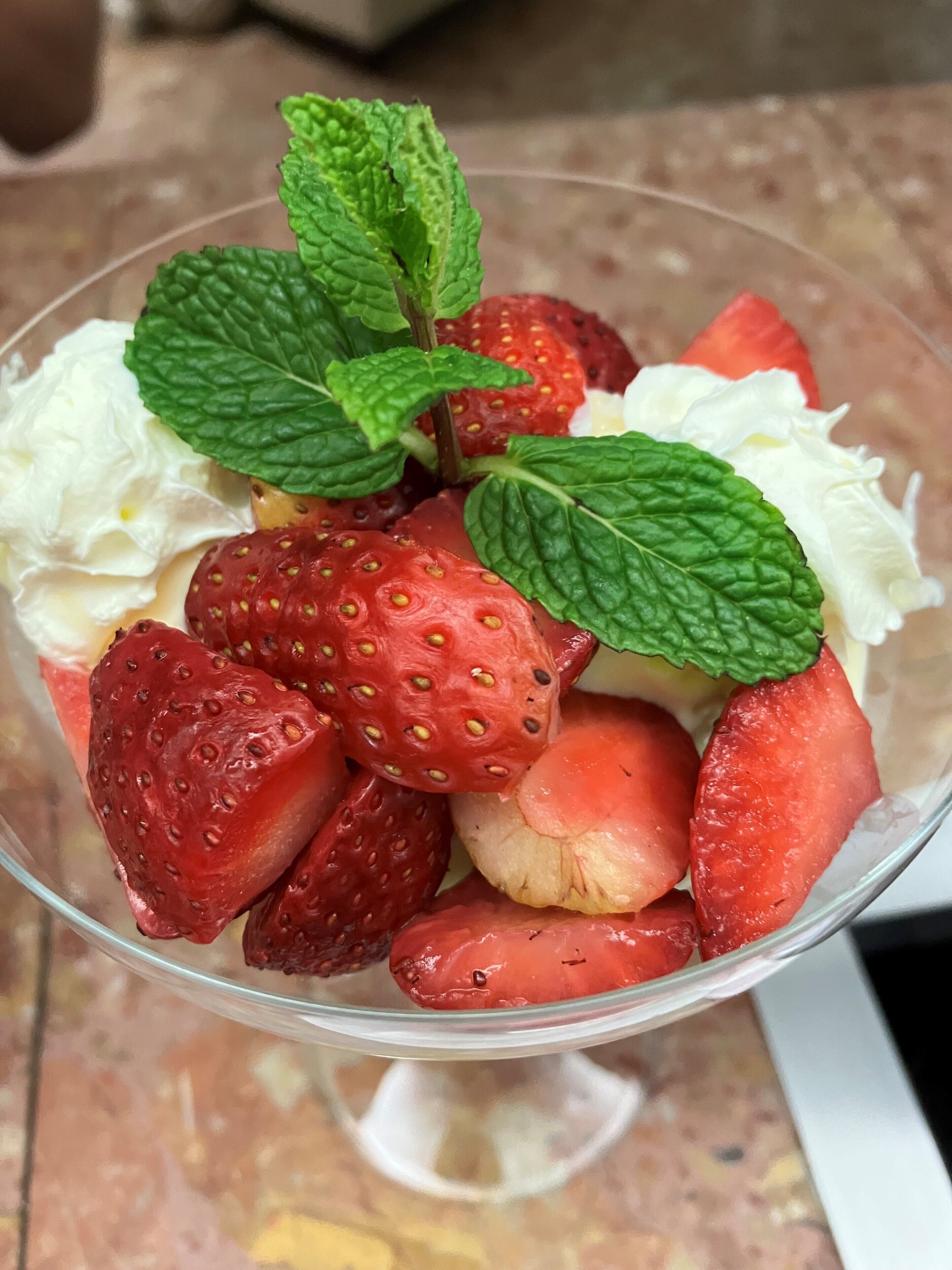 A dessert bowl with strawberries, mint leaves, and whipped cream.