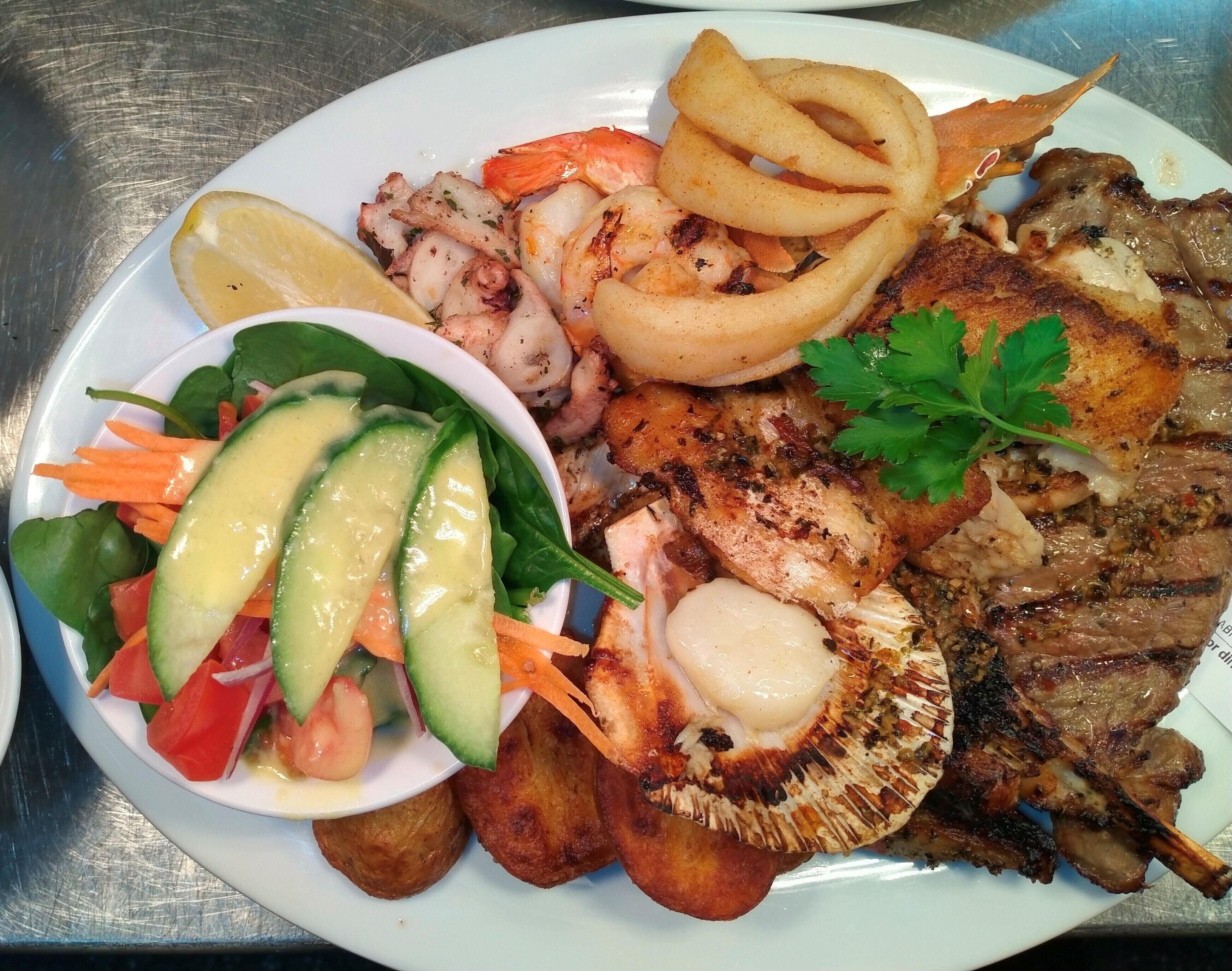 Un plato de comida con carne a la parrilla, camarones, aros de cebolla y una ensalada de verduras.