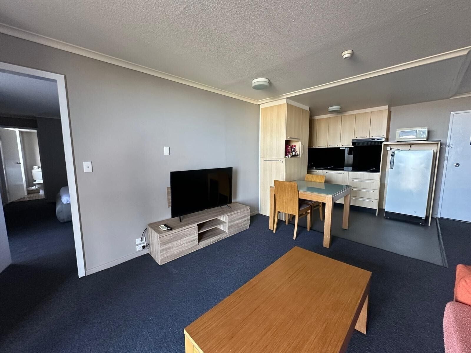 A compact living space with a television, a dining table, and a kitchenette.