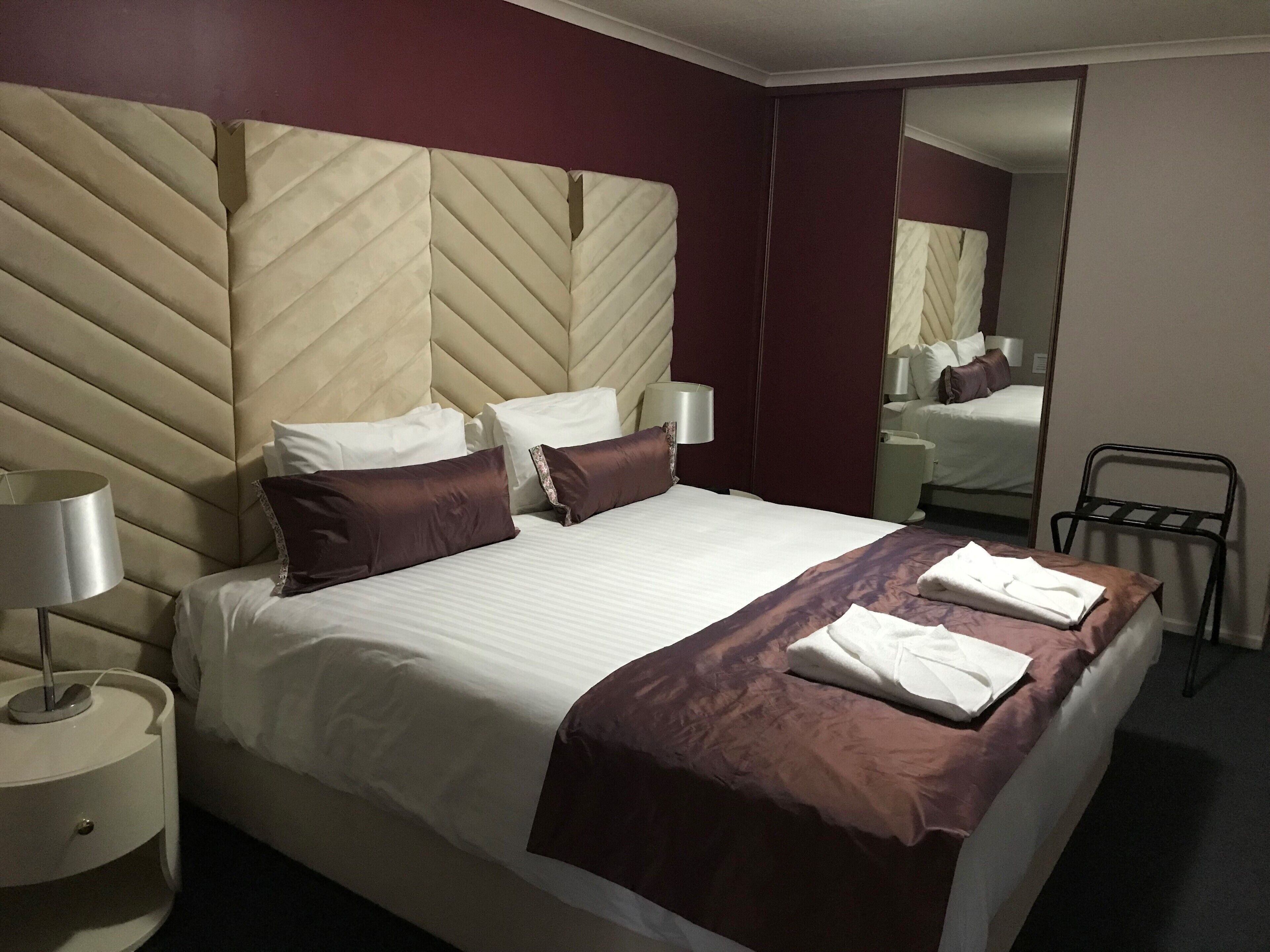 Habitación de hotel con una cama grande, una mesita de noche con lámpara, un espejo y una silla.
