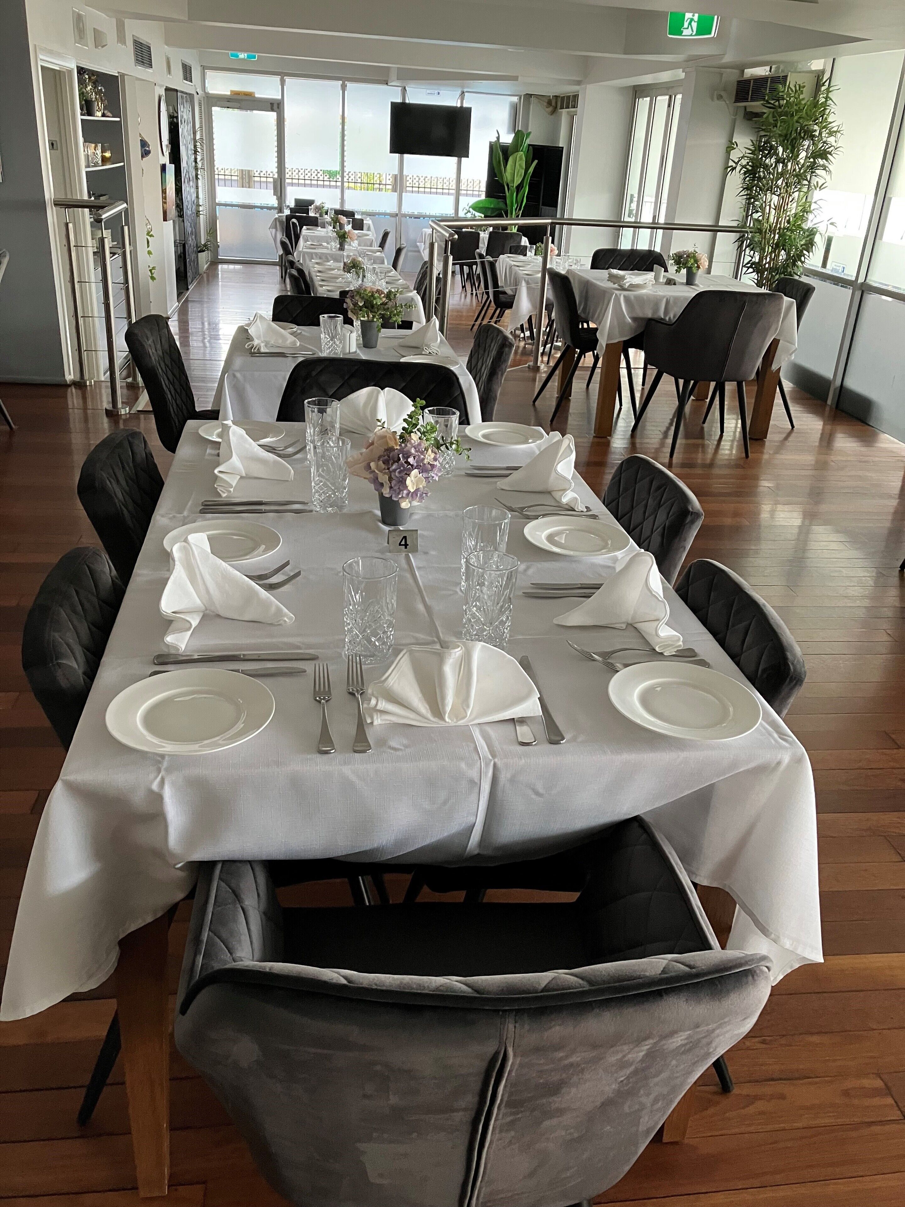A dining area with a long table set for six, surrounded by black chairs.