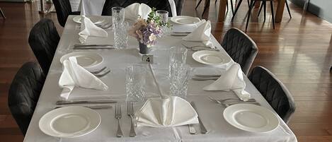 A dining area with a long table set for six, surrounded by black chairs.