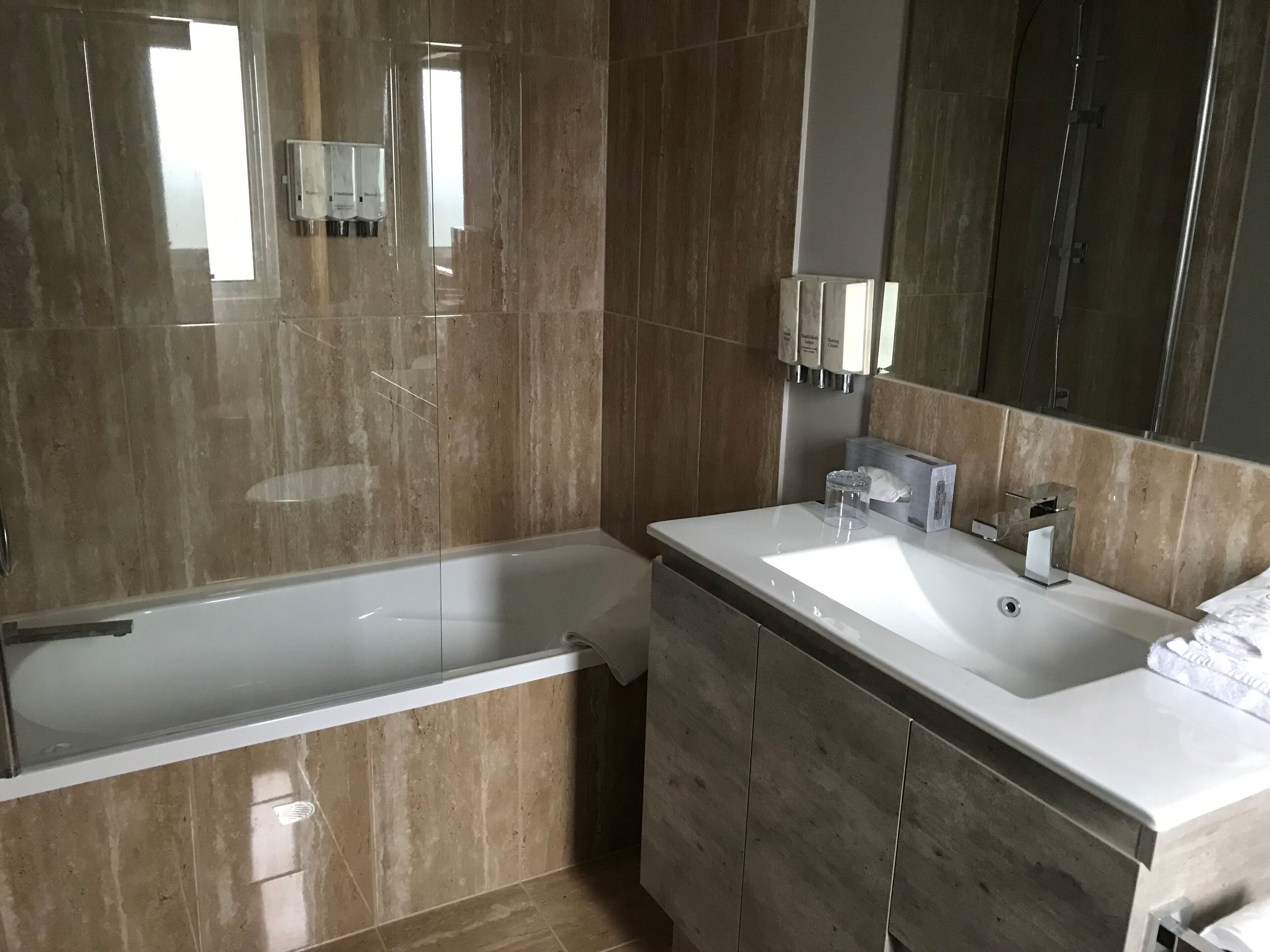 A modern bathroom with a bathtub, a large mirror, and a vanity with a sink.