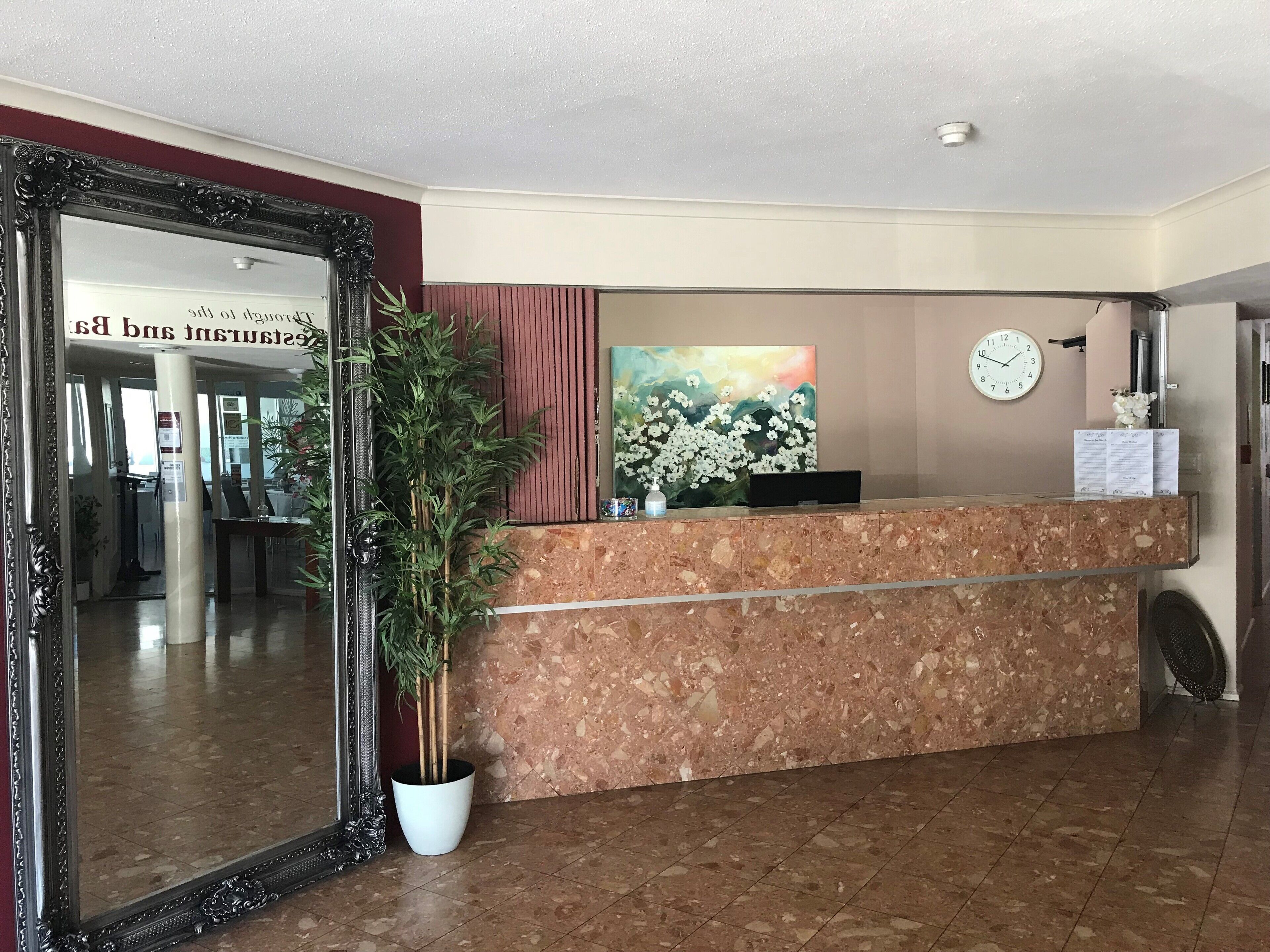 A reception desk with a clock, a framed mirror, and a potted plant.