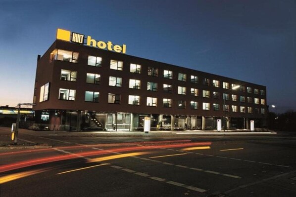 Un edificio moderno de hotel con un llamativo letrero 'KULT hotel', varios pisos y una fachada bien iluminada.