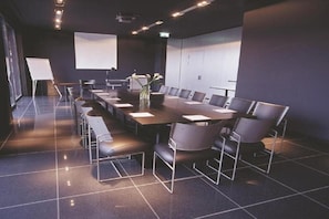 Une salle de conférence équipée d’une longue table, de chaises, d’un écran de projection et d’un tableau blanc.