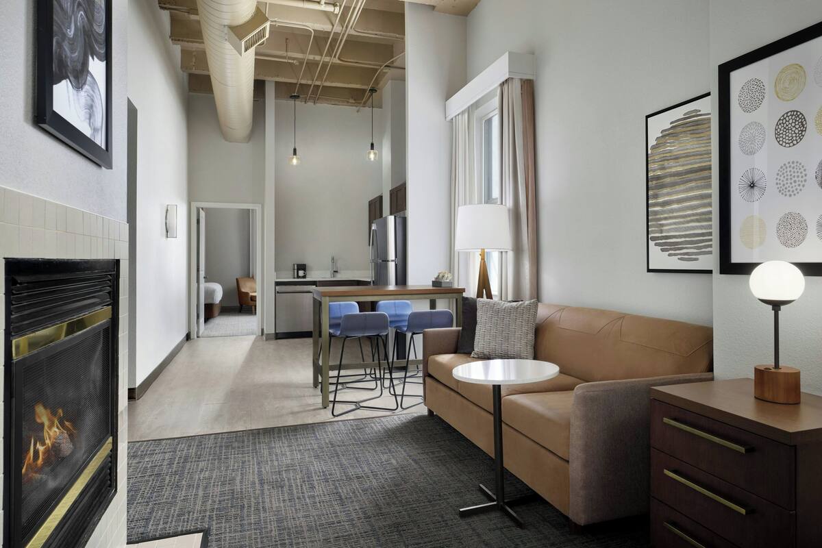 A modern living room with a fireplace, a sofa, a coffee table, and a dining area with chairs.