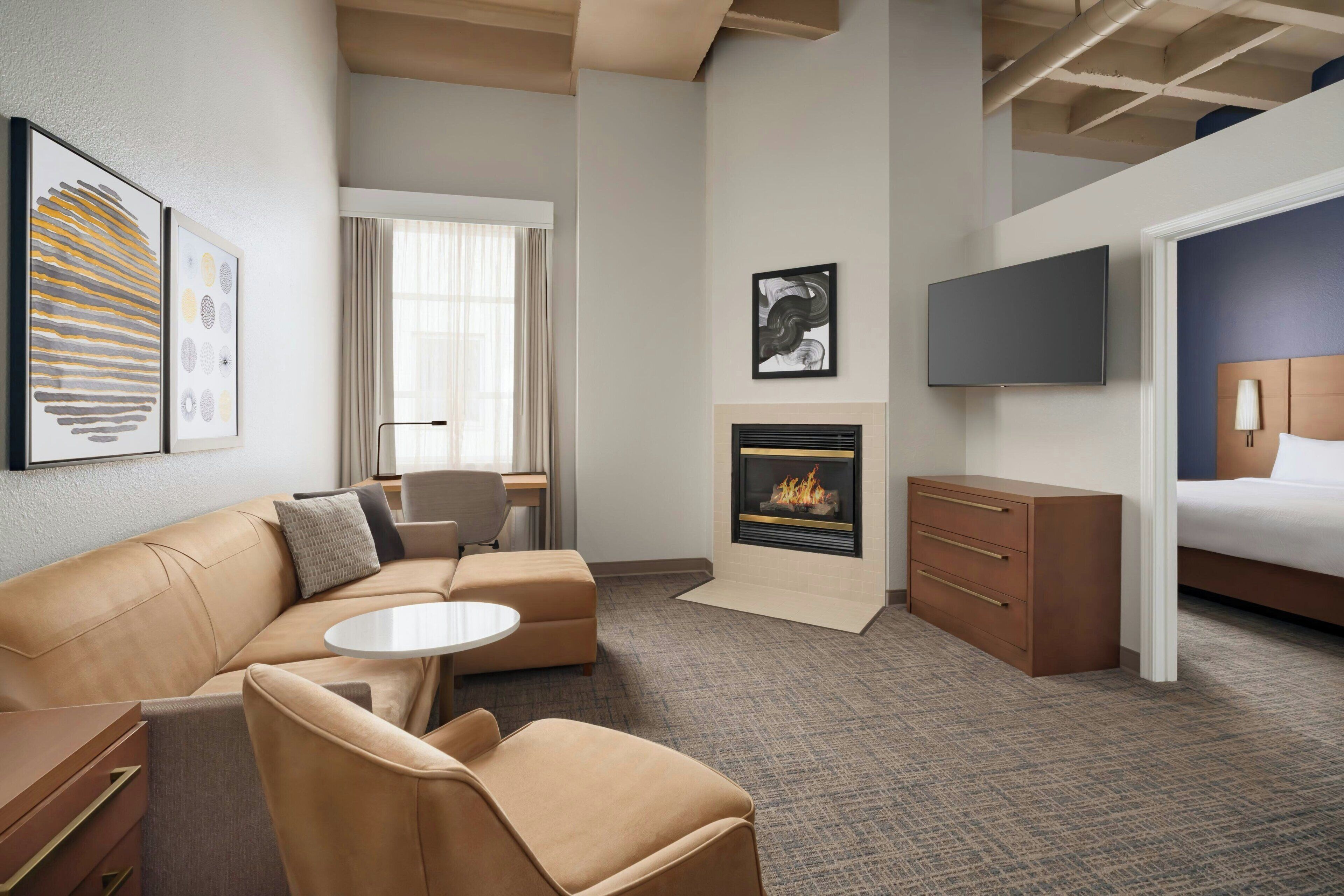 A hotel room with a sofa, a small table, a fireplace, a TV, and a bed.