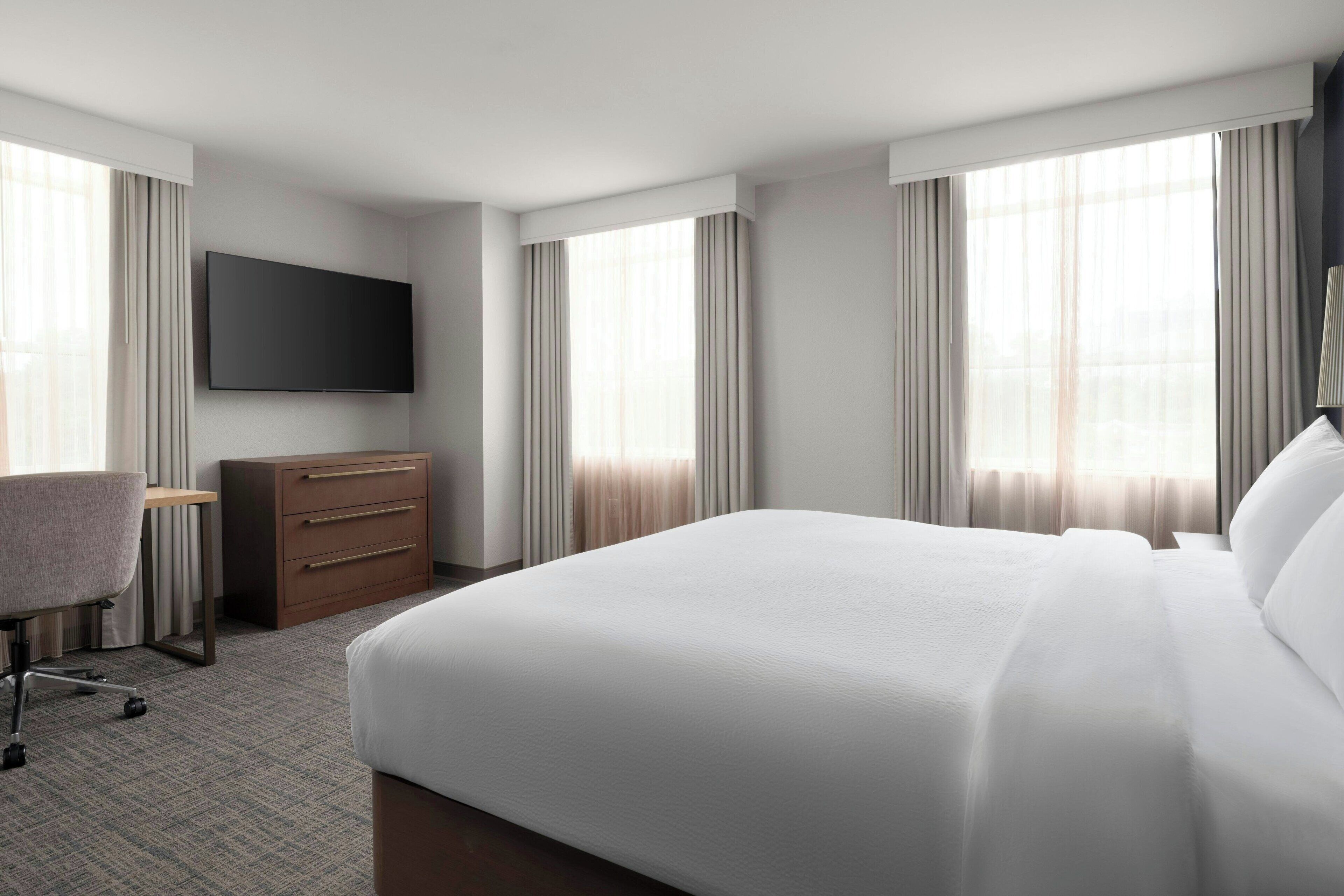 A hotel room with a large bed, a flat-screen TV mounted on the wall, a desk with a chair, and a dresser.