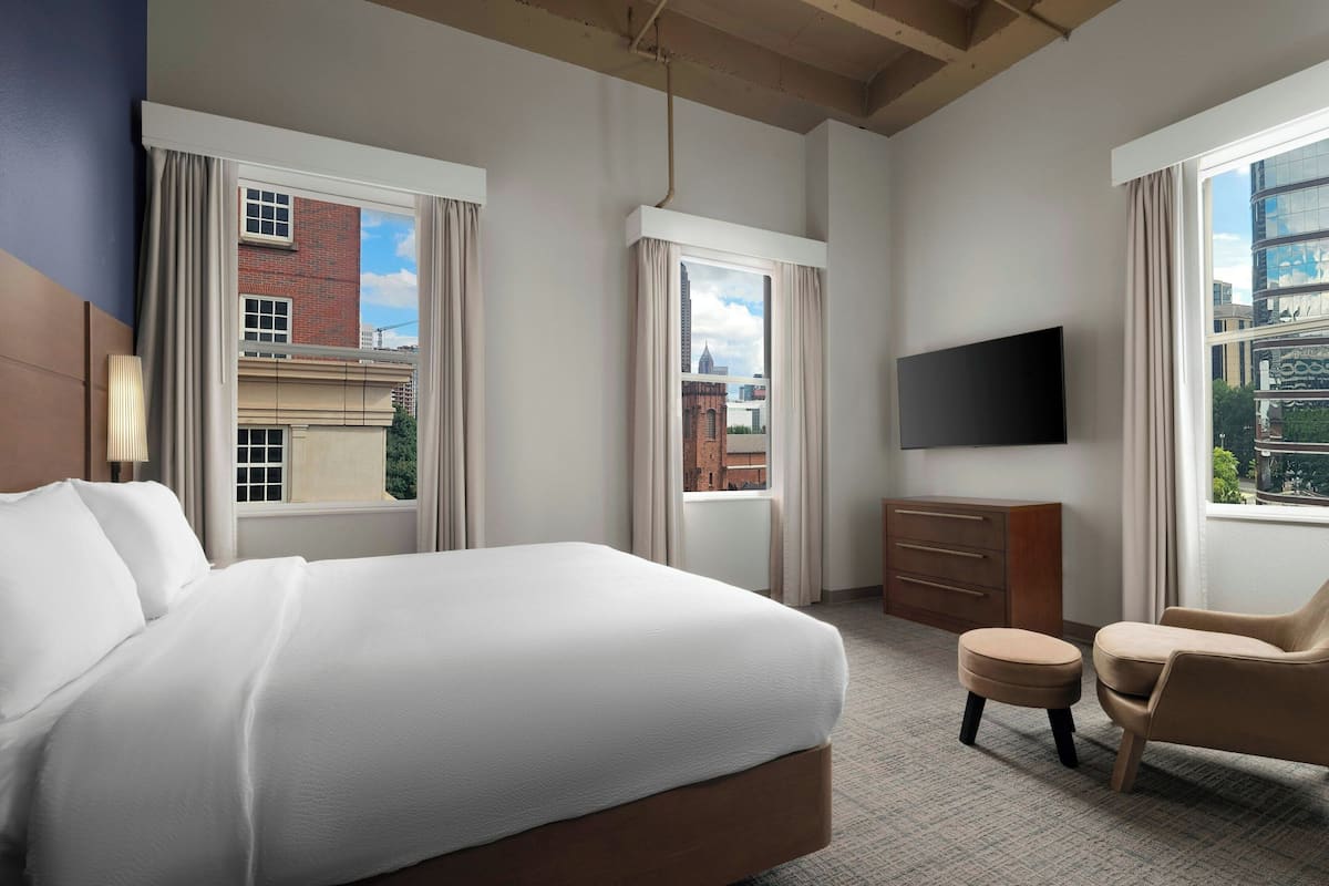A hotel room with a large bed, a TV, a chair, and a dresser.
