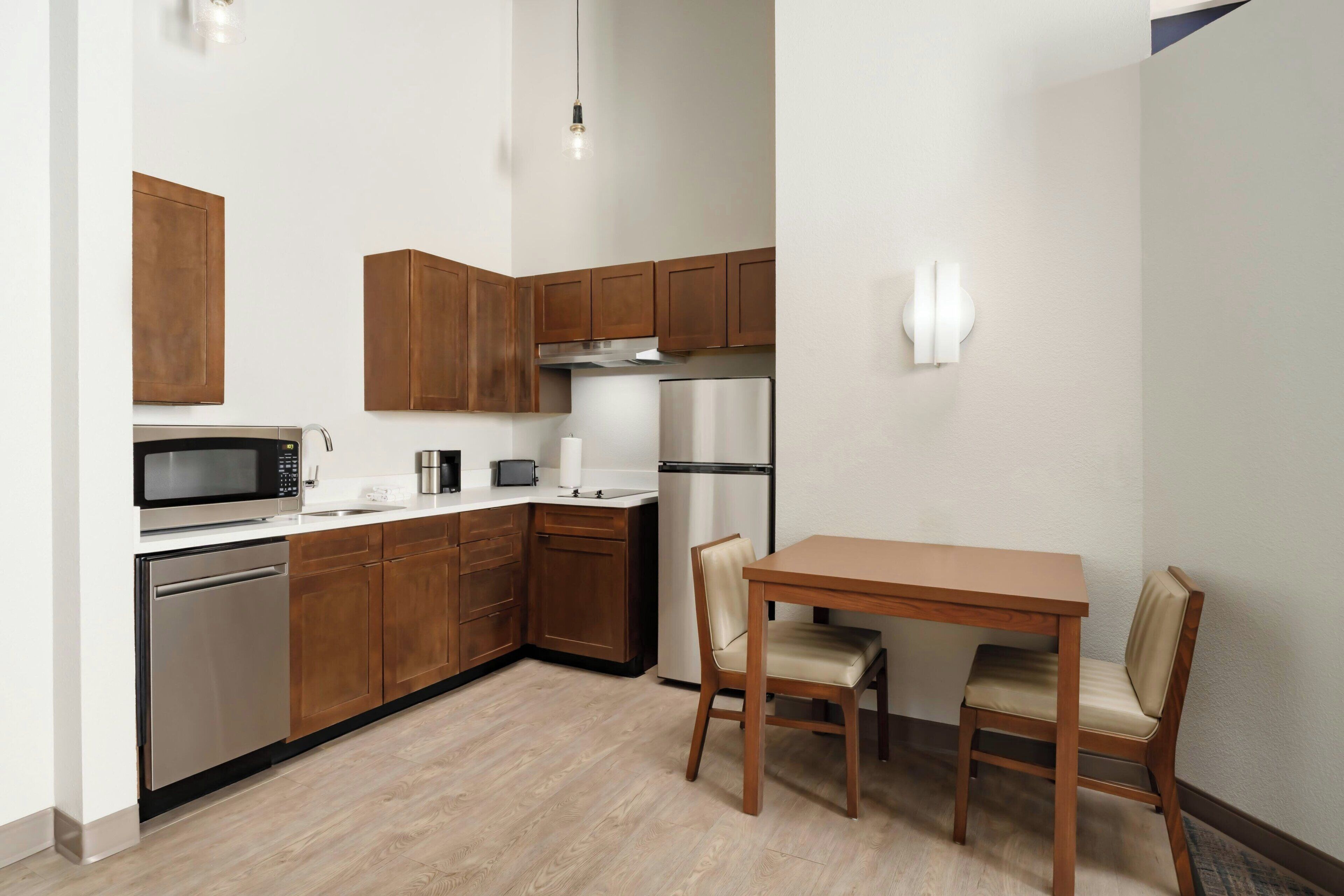 A compact kitchen with wooden cabinets, a microwave, a refrigerator, and a dining table with chairs.